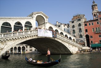 ITALY, Veneto, Venice, Gondolas carrying sightseeing tourists pass under the Rialto Bridge lined