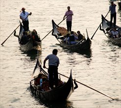 ITALY, Veneto, Venice, Gondoliers carrying sightseeing tourists on their gondolas at sunset on the