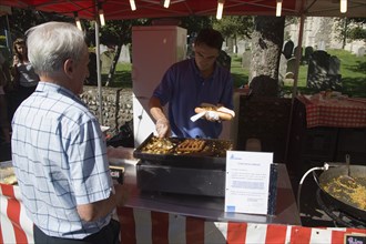 ENGLAND, West Sussex, Shoreham-by-Sea, French Market. Food stall with stallholder cooking sausage