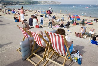 ENGLAND, Dorset, Swanage Bay, People sitting on red and white striped deckchairs looking out
