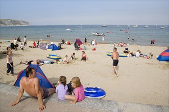 ENGLAND, Dorset, Swanage Bay, A man sat with small children looking out towards busy sandy beach