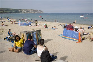 ENGLAND, Dorset, Swanage Bay, Busy sandy beach with sunbathers on the sand near deckchairs and