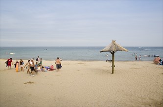 ENGLAND, Dorset, Swanage Bay, Sandy beach with sunbathers on sand near a tiki hut shade