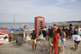 ENGLAND, Dorset, Swanage Bay, A group of children gathered near a traditional red phone box