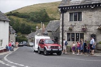 ENGLAND, Dorset, Corfe, People walking along pavements next to traditional cottages by a road with