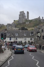 ENGLAND, Dorset, Corfe, View from road with traffic towards cottages overlooked by Corfe Castle