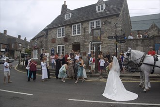 ENGLAND, Dorset, Corfe, A wedding party gathered on the street taking photographs of the bride near