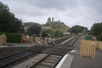 ENGLAND, Dorset, Corfe, People walking over the train line crossing with Corfe Castle behind