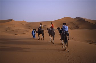 MOROCCO, Sahara, Merzouga, People camel trekking in desert surrounded by sand dunes