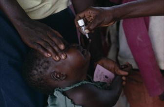 UGANDA, Medical, Health worker administering immunization polio drops to child in area near Gulu.