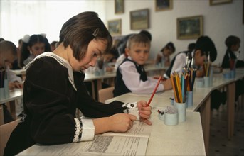 KAZAKHSTAN, Astana, Young female student writing in classroom of boys and girls.