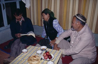 UZBEKISTAN, Tashkent, "Uzbek family sat around tablke, with one man reading a book."
