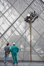 FRANCE, Ile de France, Paris, Workmen watching robot window cleaning machine on the pyramid at the