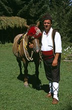 BULGARIA, Chalin Valog, "Man in national costume standing with horse. Pirin Mountain, near Bansko,.