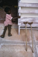 TANZANIA, Medical, Child with both legs in braces sitting in open doorway of polio unit beside pair