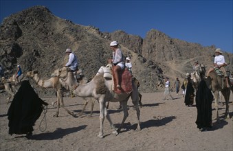 EGYPT, Eastern Desert, Bedouin women dressed in black leading tourists along on camels