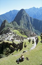 PERU, Cusco Department, Machu Picchu, "Inca ruins, terraces, visitor sitting on terrace, and Huayna