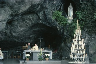 FRANCE, Midi-Pyrenees, Hautes-Pyrenees, Lourdes.  Priest conducting service at cave shrine in