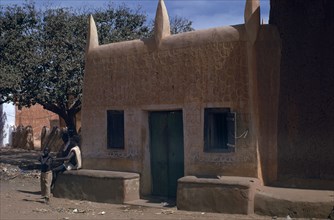 NIGERIA, Kano, Traditional mud brick Hausa dwelling with men and boy beside exterior wall.