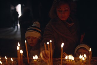 ARMENIA, Echmiadzin, Woman and child lighting candles inside church on Christmas day.
