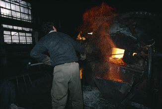 ARMENIA, Yerevan, Cable factory worker in front of furnace with flying sparks.