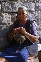 BULGARIA, Bansko, Old lady sitting on bench knitting.