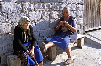 BULGARIA, Bansko, Two old ladies sitting on bench knitting.