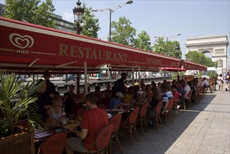 FRANCE, Ile de France, Paris, Tourists eating lunch at tables under shade in the Champs Elysees