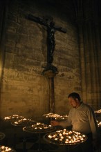FRANCE, Ile de France, Paris, Man lighting votive candles below a cross with Christ crucified in a