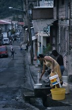 ST LUCIA, Soufriere, Man and woman collecting water from standpipe in narrow street with open