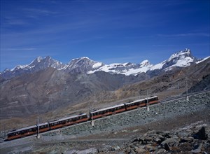 SWITZERLAND, Valais, Zermatt, "Gornegrat Railway with train traveling past snow capped mountains