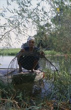 EGYPT, Luxor, Nile Fisherman crouching down next to river bank on the West Bank under tree branches