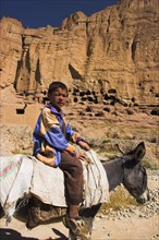 AFGHANISTAN, Bamiyan Province, Bamiyan , Boy on donkey infront of caves in cliffs near empty niche