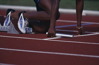 20085197 SPORT Athletics Running Detail of lower half of a runner holding a batton in a relay race with feet in the starting blocks