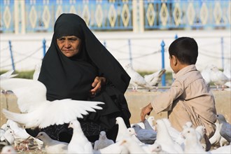 AFGHANISTAN, Mazar-I-Sharif, "Lady wearing burqa and son feeding famous white pigeons at Shrine of