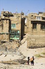 AFGHANISTAN, Ghazni, "Children walk with sacks over their shoulders toward houses inside the