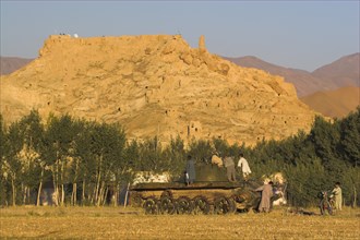 AFGHANISTAN, Bamiyan Province, Bamiyan, "Children playing on abandoned tanks in fied in front of