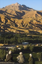 AFGHANISTAN, Bamiyan Province, Bamiyan, Men sit above Bamiyan village as the late afternoon sun