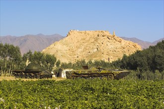 AFGHANISTAN, Bamiyan Province, Bamiyan, "Abandoned tanks in fied in front of Ruined citadel of