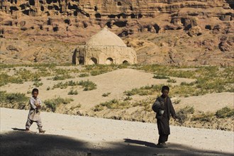 AFGHANISTAN, Bamiyan Province, Bamiyan, Boys walk past tomb near empty niche where the famous