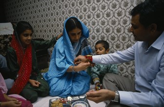 ENGLAND, Religion, Hindu, Woman tying thread on wrist of man during the Sacred Thread ceremony. The