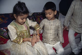 ENGLAND, Religion, Hindu, Young girl tying a thread to the wrist of a young boy during the Sacred