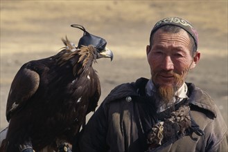 MONGOLIA, People, Head and shoulders portrait of Kazakh nomad man with golden eagle wearing hood