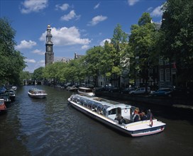 HOLLAND, Noord-Holland, Amsterdam, Pleasure boats on canal lined by trees and parked cars on side