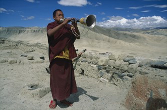 NEPAL, Mustang, Namgyal Gompa, "Tibetan Buddhist monk blowing long, decorated horn on monastery