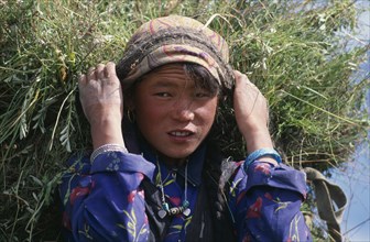 NEPAL, Mustang, Lo Manthang, Portrait of young girl carrying load of harvested grasses supported by