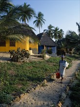 TANZANIA, Pangani, The Tides Hotel.  Brightly painted thatched huts amongst palm trees with maid