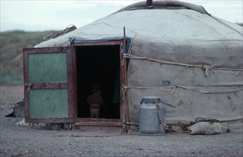 MONGOLIA, Architecture, Young child standing inside open doorway of yurt wearing just a jumper and