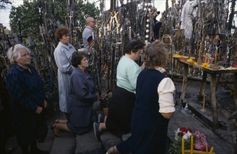 LITHUANIA, Hill of Crosses, Men and women pray in front of hundreds of crosses and crucifix at