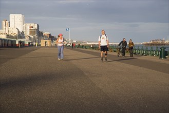 ENGLAND, East Sussex, Brighton, Woman jogging with man rollerblading on the seafront promenade.